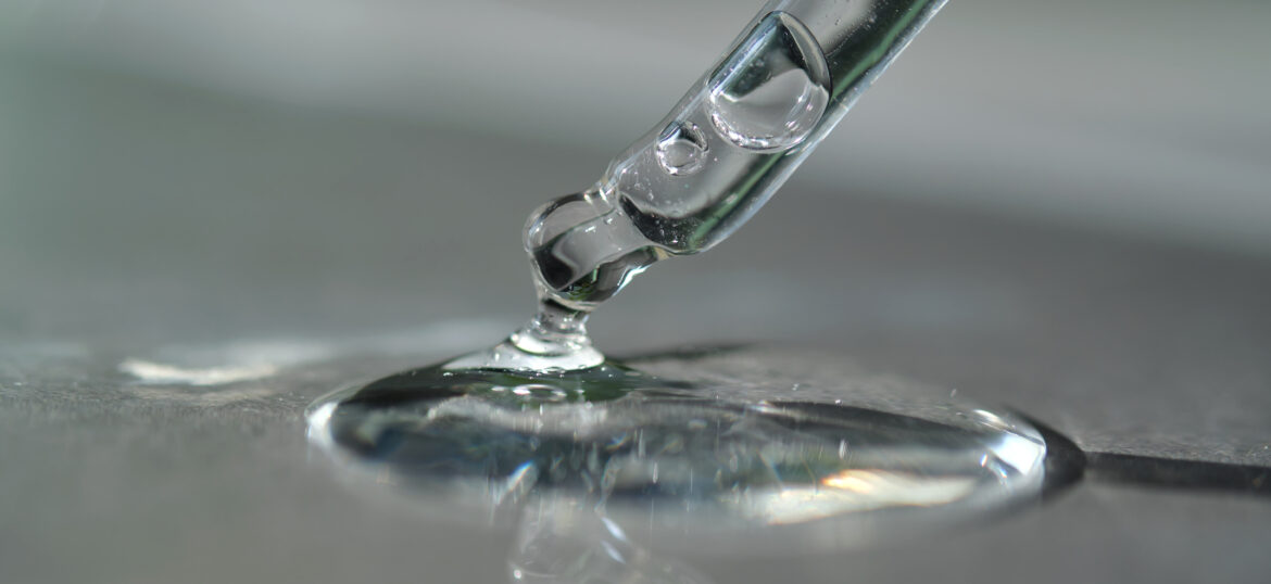 Pipette with spilled cosmetic oil or serum on a gray background.