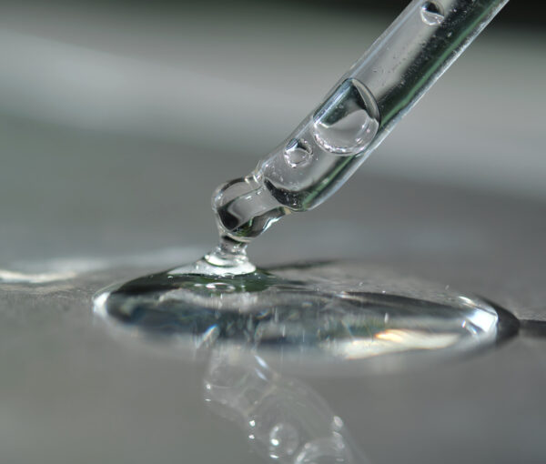 Pipette with spilled cosmetic oil or serum on a gray background.