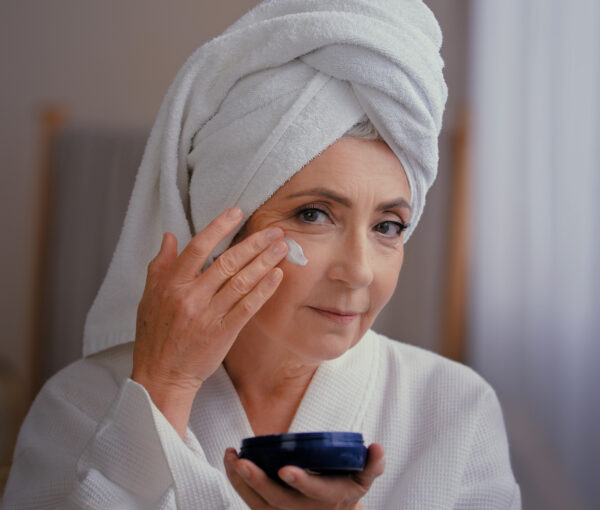 Portrait beautiful Caucasian old 60s woman 50s lady grandmother aged model with towel on head face care facial lifting hydration applies moisturizing natural anti-wrinkles cream with collagen in bath